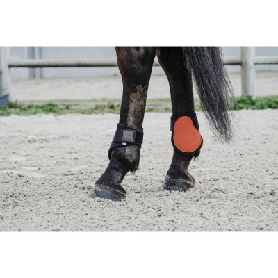 Patas traseiras de cavalo com protetores de equitação laranja e preto sobre areia clara