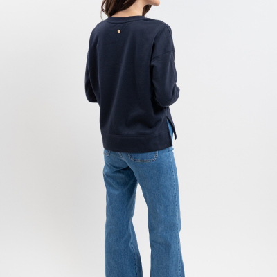 Mulher de costas com sweatshirt azul escuro, calças de ganga largas e ténis brancos