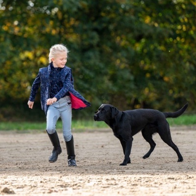 Criança com casaco azul corre na praia junto a um cão preto