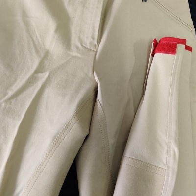 Calças bege Euro-Star com bolso e detalhes vermelhos, sobre outras roupas