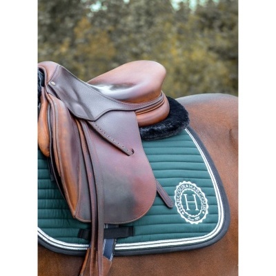 Sela de couro castanha sobre cavalo com mantilha verde escura e logo 'H'