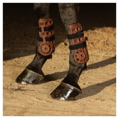 Pernas de cavalo com botas de proteção marrons e tiras pretas numa superfície arenosa