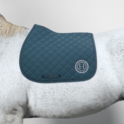 Têxtil acolchoado azul escuro com padrão em losangos e logo HARCOUR sobre cavalo branco com manchas