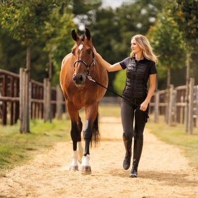 Mulher de colete preto a conduzir cavalo castanho numa pista de areia
