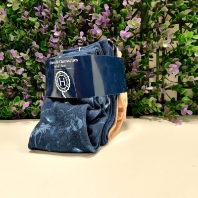 Conjunto de meias azul e bege com embalagem azul escura e vegetação ao fundo