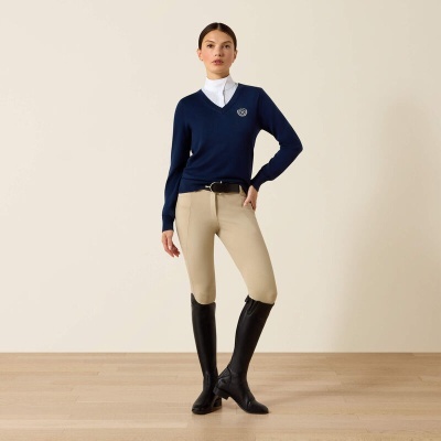 Mulher com camisola azul, camisa branca, calças bege e botas pretas
