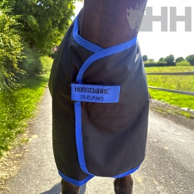 Capa para cavalo preta com bordas azuis e etiqueta azul em estrada rural