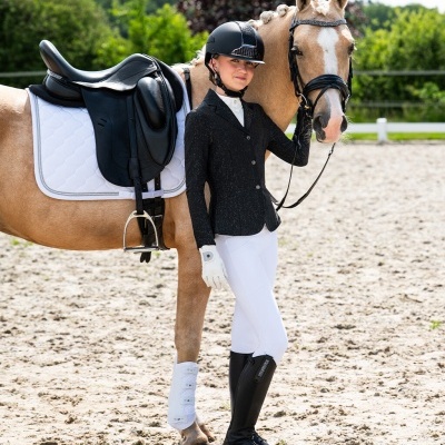 Cavaleira com equipamento preto e branco junto a cavalo castanho claro em picadeiro ao ar livre
