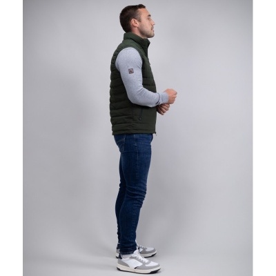 Homem de perfil a vestir colete verde escuro, camisa cinzenta, jeans e ténis brancos