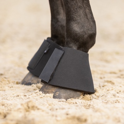 Proteções pretas de neoprene nas patas de um cavalo na areia