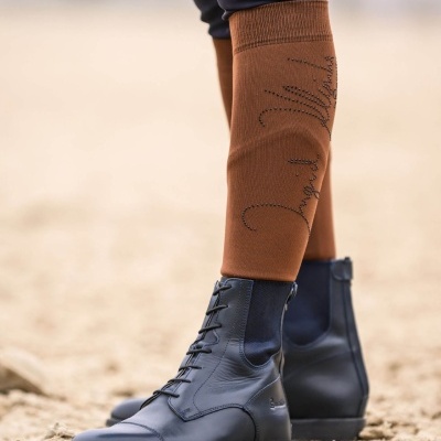 Botas de couro preto com atacadores e perneiras castanhas com escrita decorativa num chão de areia.