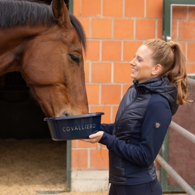 Mulher a alimentar cavalo com taça azul COVALLIERO num estábulo