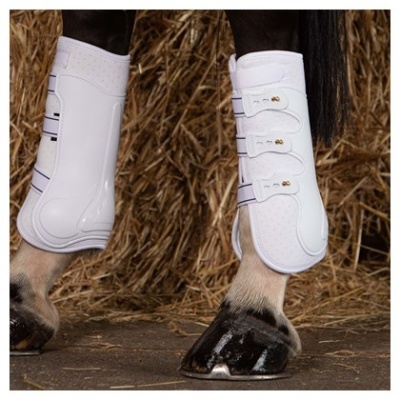 Pernas de cavalo com proteções brancas e fivelas, piso de terra e feno ao fundo