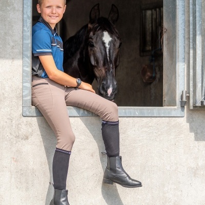 Jovem com roupas de equitação sentado na moldura de janela de estábulo com cavalo preto