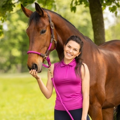 Mulher com cavalo castanho e acessórios rosas em ambiente natural