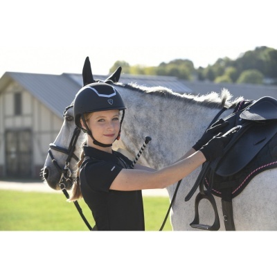 Jovem cavaleira com capacete, luvas e cavalo com sela preta em ambiente exterior