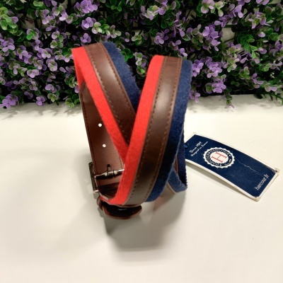 Cinto tricolor em azul, castanho e vermelho com fivela metálica, etiqueta e fundo de flores lilases.