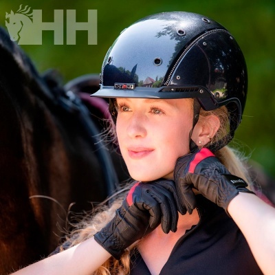 Mulher jovem a usar capacete de equitação preto e luvas com cavalo ao fundo