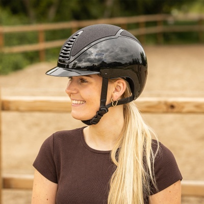 Capacete de equitação preto com pormenores cinzentos usado por mulher loira