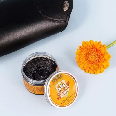 Creme para polir sapatos SHOE POLISH com tampa ao lado, flor laranja e sapato preto de couro