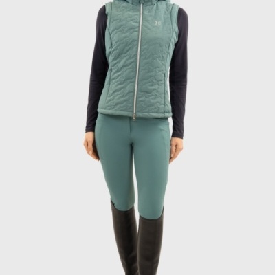 Mulher com colete verde com capuz, camisola preta, leggings verdes e botas pretas