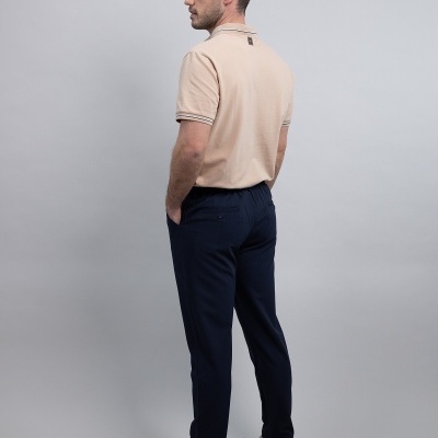 Homem de costas com polo bege e calças azuis escuras em fundo cinzento