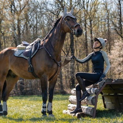 Cavalo castanho com sela e mulher com roupa de equitação ao ar livre