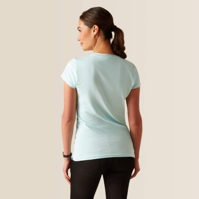 Mulher de costas com t-shirt azul claro e calças pretas, fundo bege claro