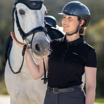 Pessoa com capacete e cavalo branco com arreio e protetor de orelhas preto