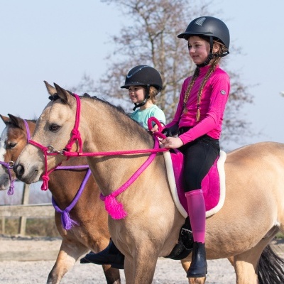 Duas raparigas a cavalgar cavalos com arreios rosa e roxo ao ar livre