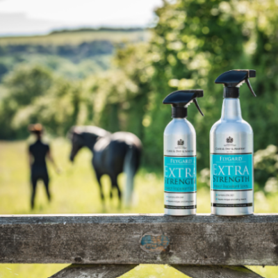 Dois frascos de spray para limpeza de cavalos sobre portão de madeira com cavalo e pessoa ao fundo