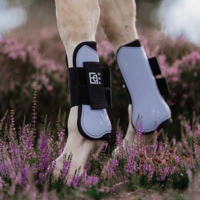 Protector de pernas de cavalo cinzento e preto com texto EQ PRO junto a flores roxas