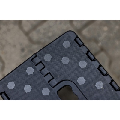 Superfície preta com padrão de hexágonos cinzentos e dobradiças num objeto sobre chão cinzento