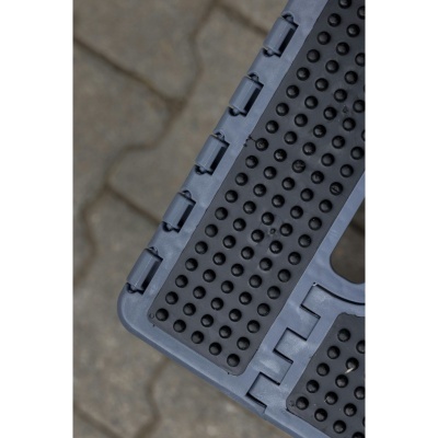 Superfície plástica cinza com textura de pontos em relevo sobre pavimento de pedras.