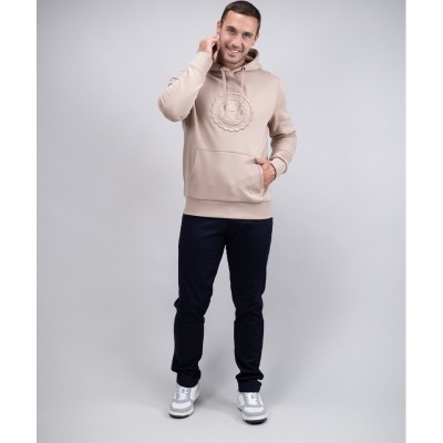 Homem com hoodie bege, calças pretas e sapatilhas brancas em fundo cinza