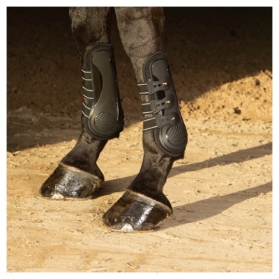 Pernas de cavalo com protetores pretos em ambiente arenoso
