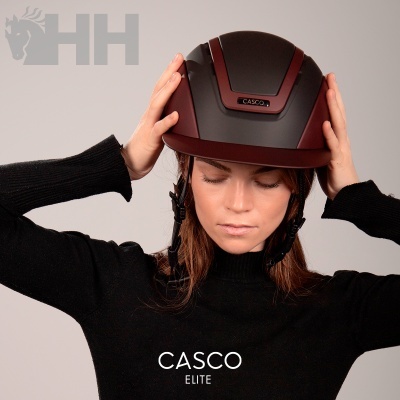 Mulher a colocar capacete preto e castanho com etiqueta CASCO, fundo cinza claro