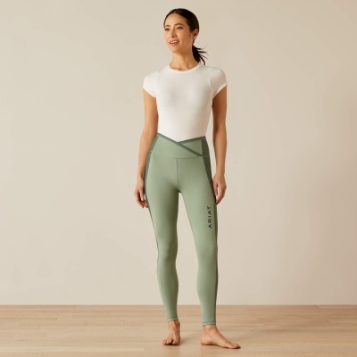 Mulher a usar leggings verdes claras com texto ARIAT e t-shirt branca em ambiente interior