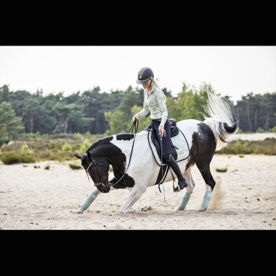 Cavalo preto e branco com cavaleiro vestido de capacete e roupa clara em terreno arenoso