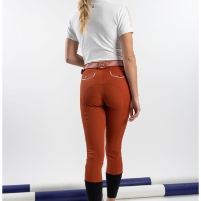 Modelo de costas com calças de equitação castanhas e polo branca num estúdio com obstáculos de equitação