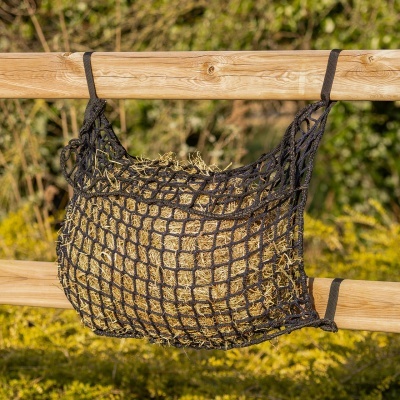 Rede alimentar preta pendurada numa cerca de madeira com feno dentro