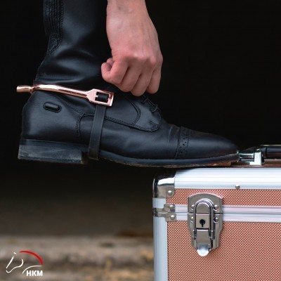 Bota de montaria preta com fivela cor de cobre junto a caixa metálica com fecho prateado