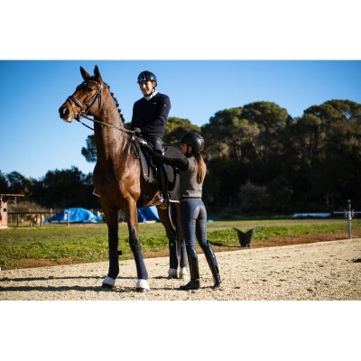 Dois cavaleiros com capacetes e roupa de equitação junto a um cavalo castanho ao ar livre