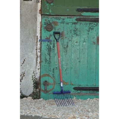 Ancinho com cabo vermelho e dentado azul junto a porta verde desgastada