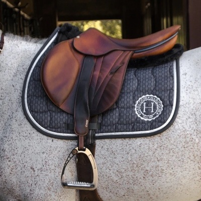 Sela de equitação em couro castanho escuro sobre cavalo branco com alforje preto e logótipo H