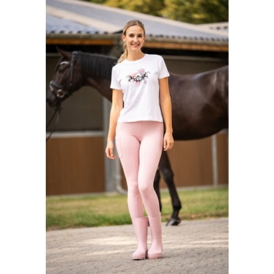 Mulher com roupa de equitação rosa e branca ao ar livre com cavalo castanho ao fundo