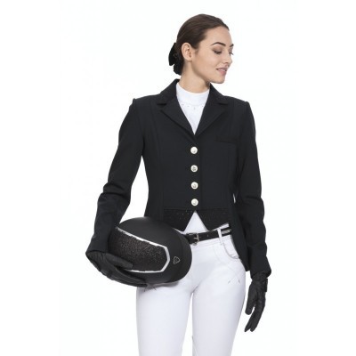 Mulher vestida com fato de competição equestre, segurando capacete preto, fundo branco.