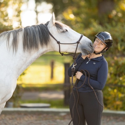 Pessoa de capacete preto e roupa azul escura com cavalo branco com rédea castanha num ambiente natural