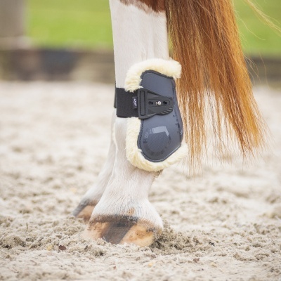 Protector para perna de cavalo cinza com forro de pele branca em perna branca numa área arenosa