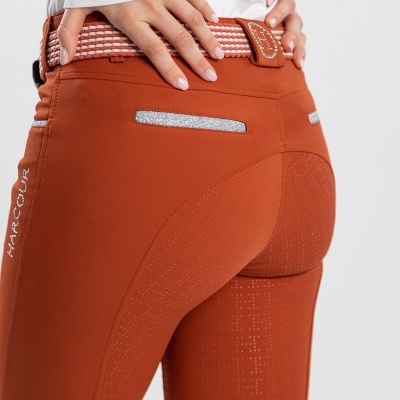 Calças justas laranja com detalhes brilhantes nos bolsos traseiros e cinto bege e laranja, com camisa branca